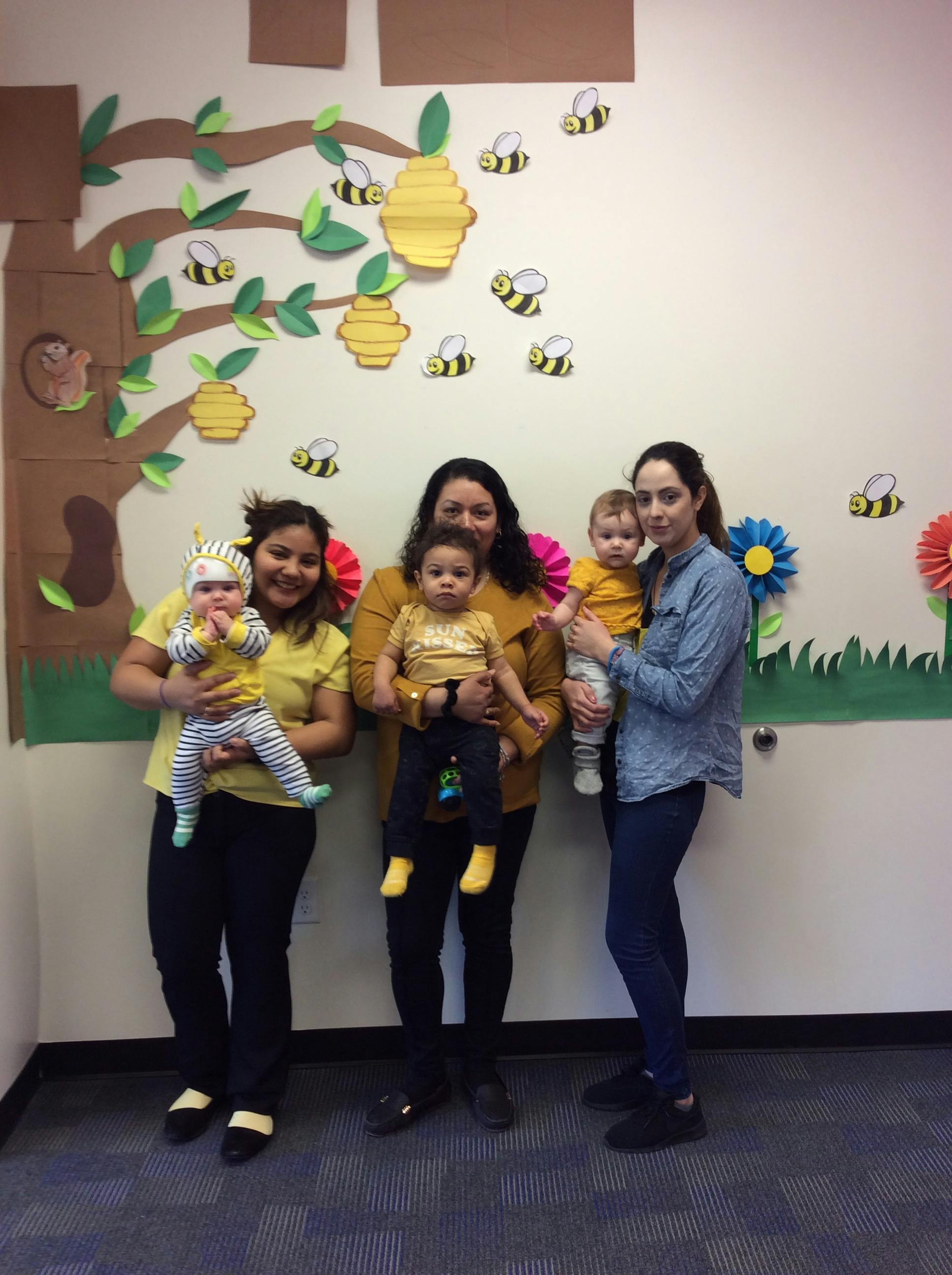 Three people holding three children in a room with bee decorations
