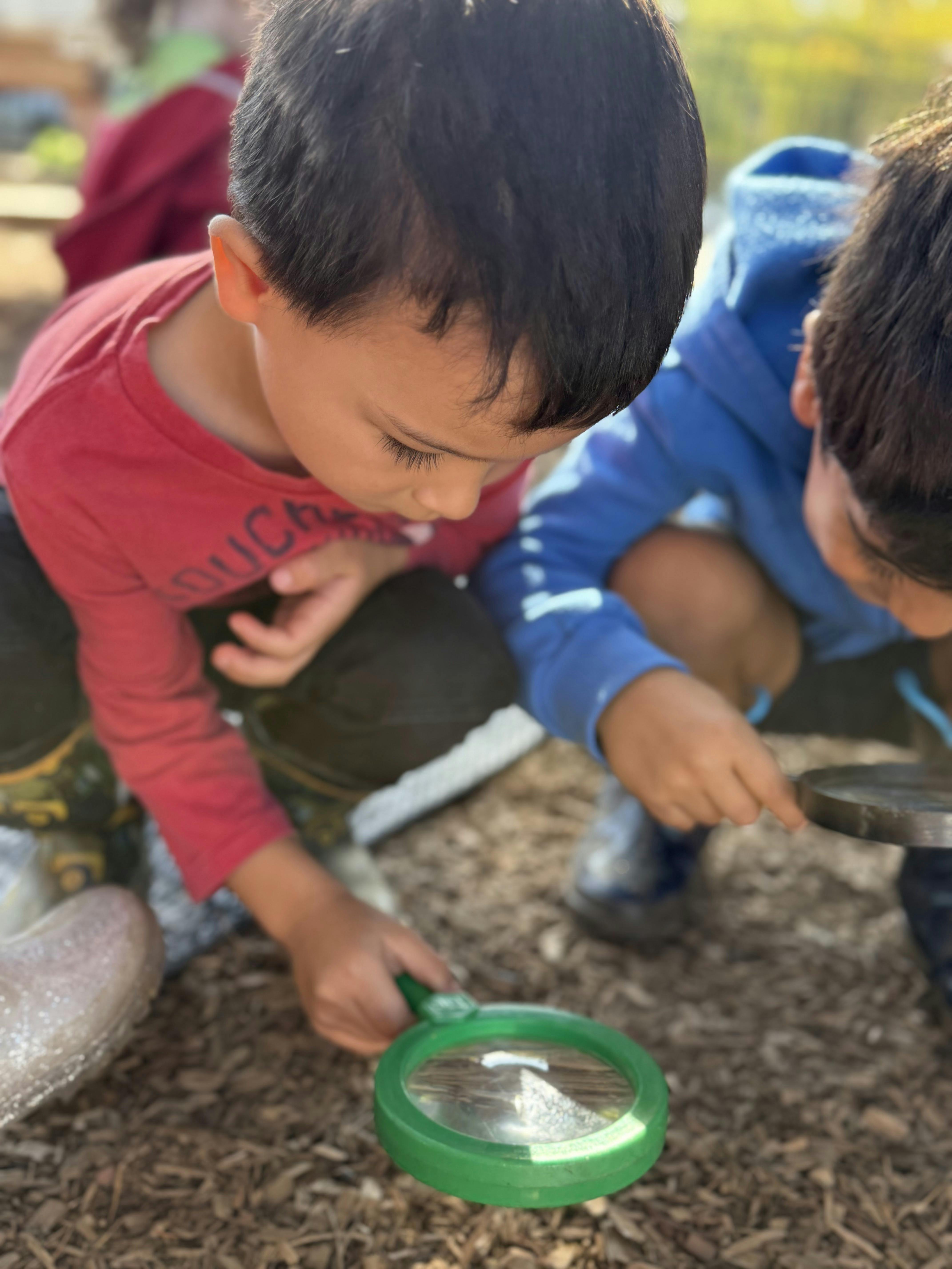 Two children looking at something on the ground with magnifying glasses