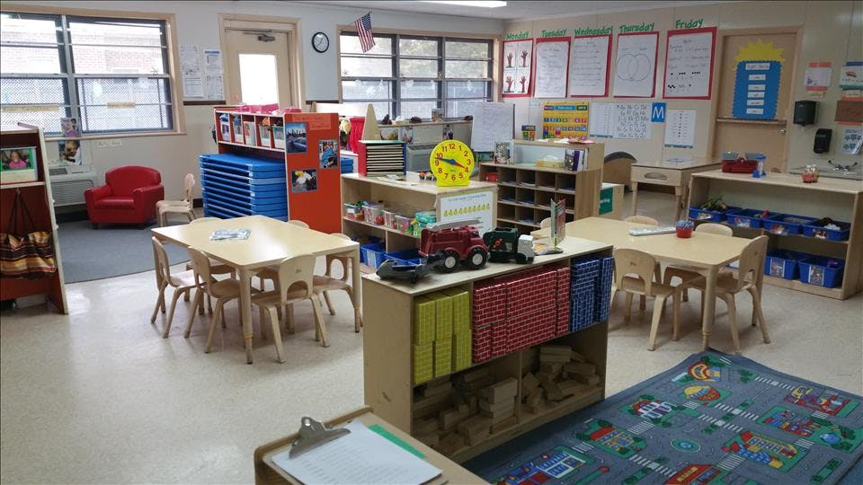 An empty classroom with small tables and chairs, shelves, and learning materials