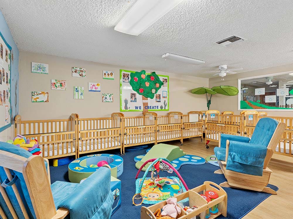 A classroom with several cribs, play mats, and a rocking chair