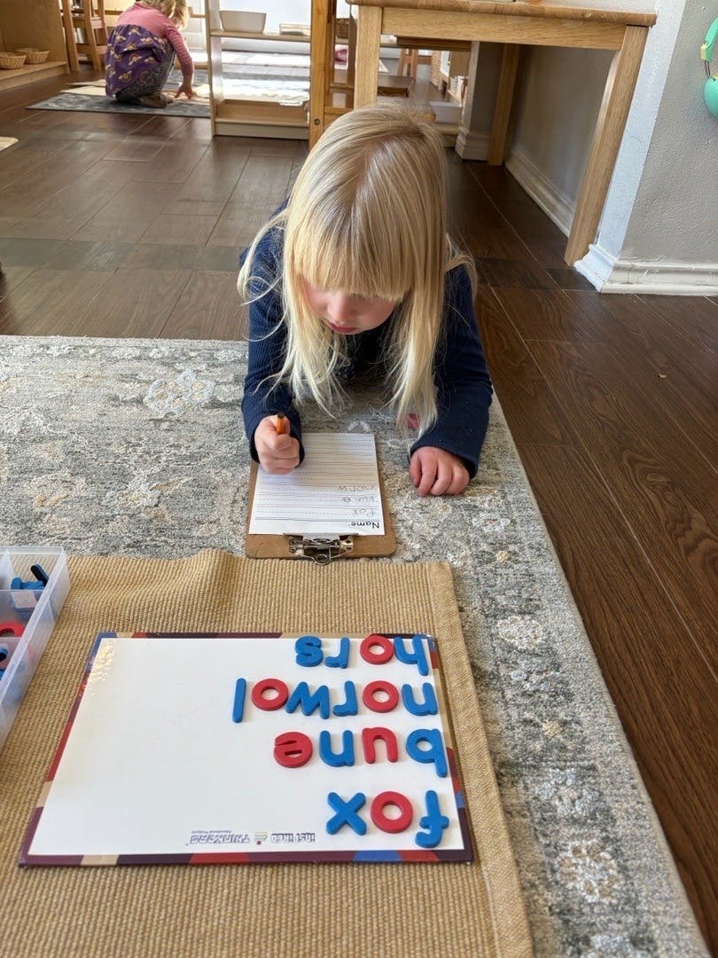 Child lying on the floor writing while looking at magnetic letters