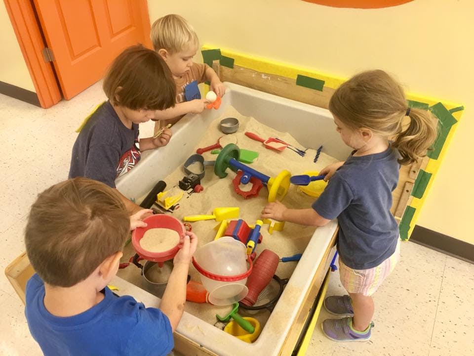 Four children playing in a sand table with toys