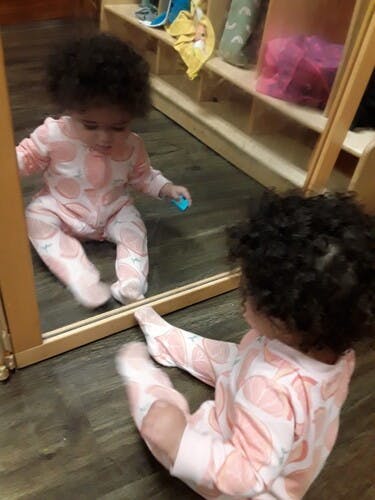 Child sitting on floor looking at reflection in mirror
