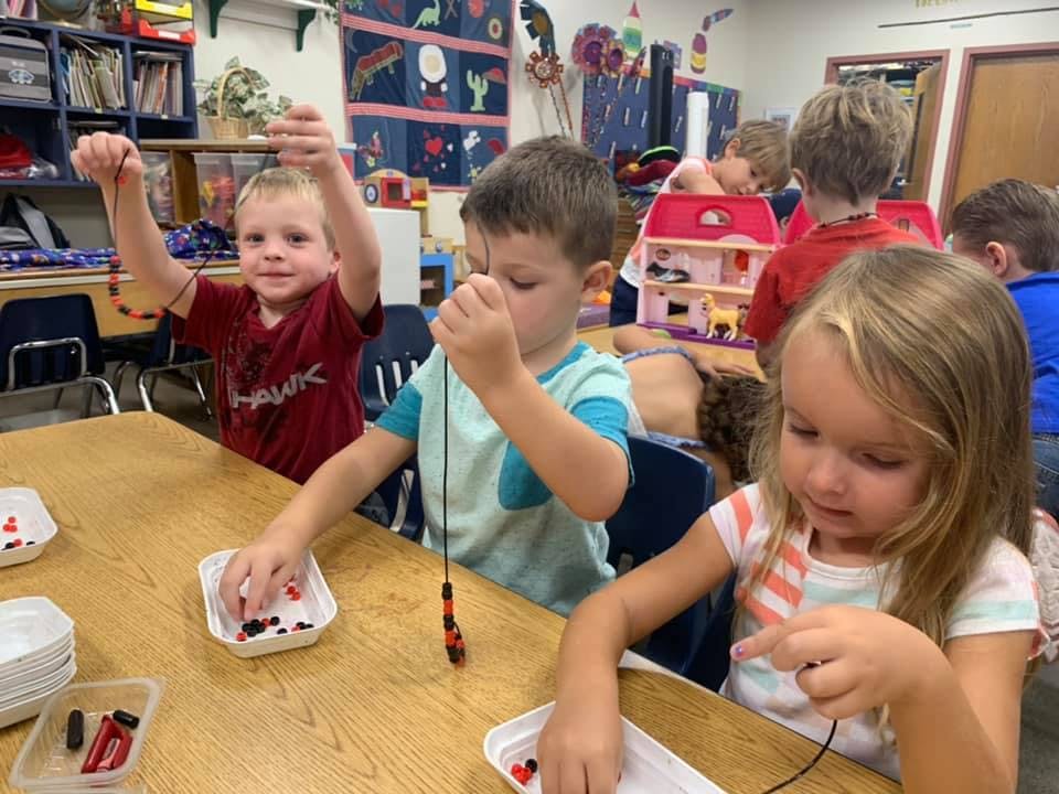 Children making beaded necklaces at a table