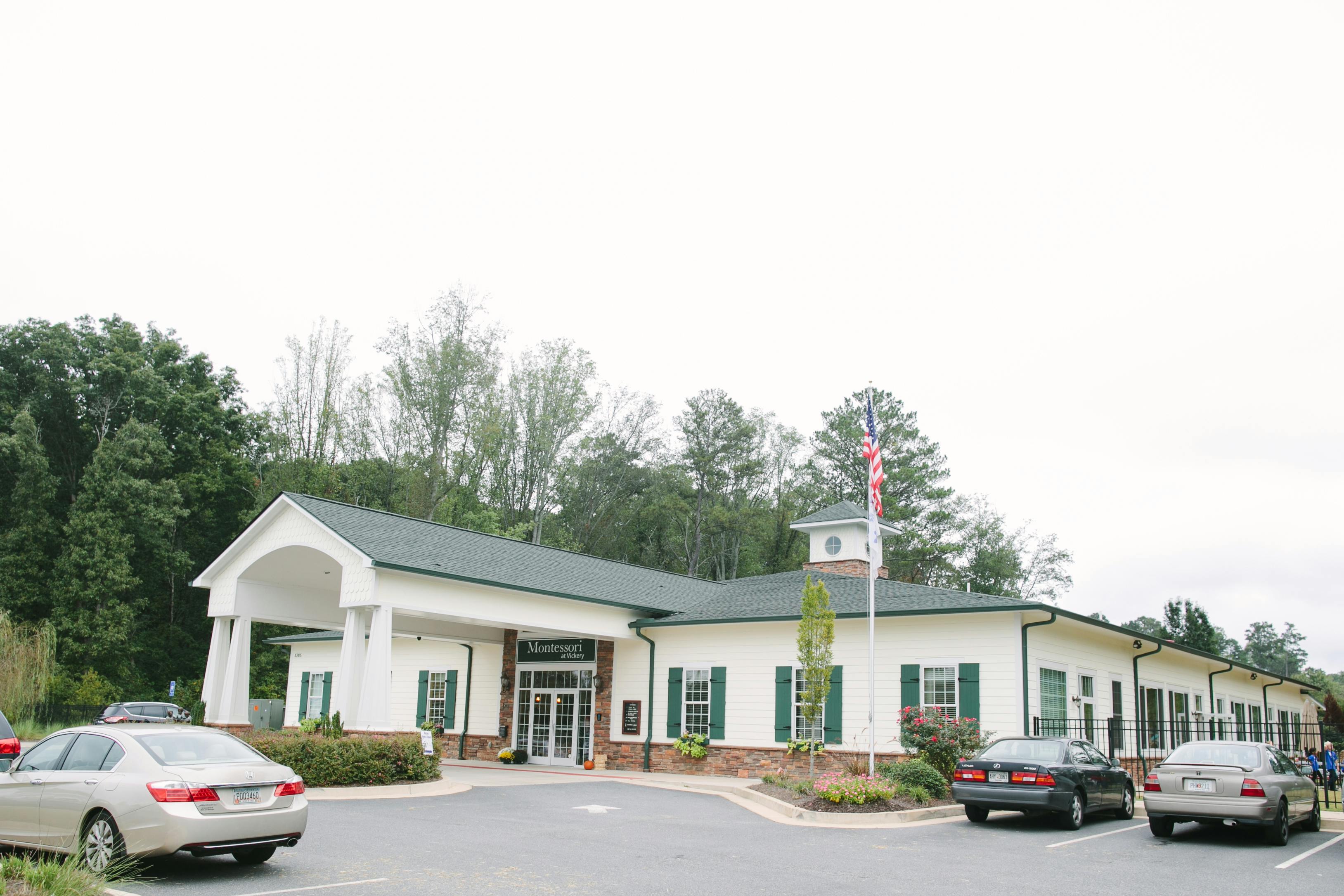 White building with green shutters and a portico, cars in a parking lot