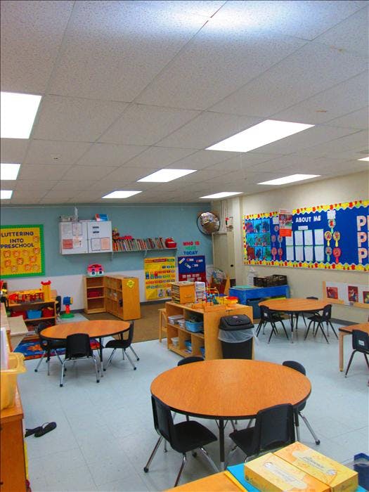 Empty classroom with small round tables and chairs, toys, and colorful bulletin boards