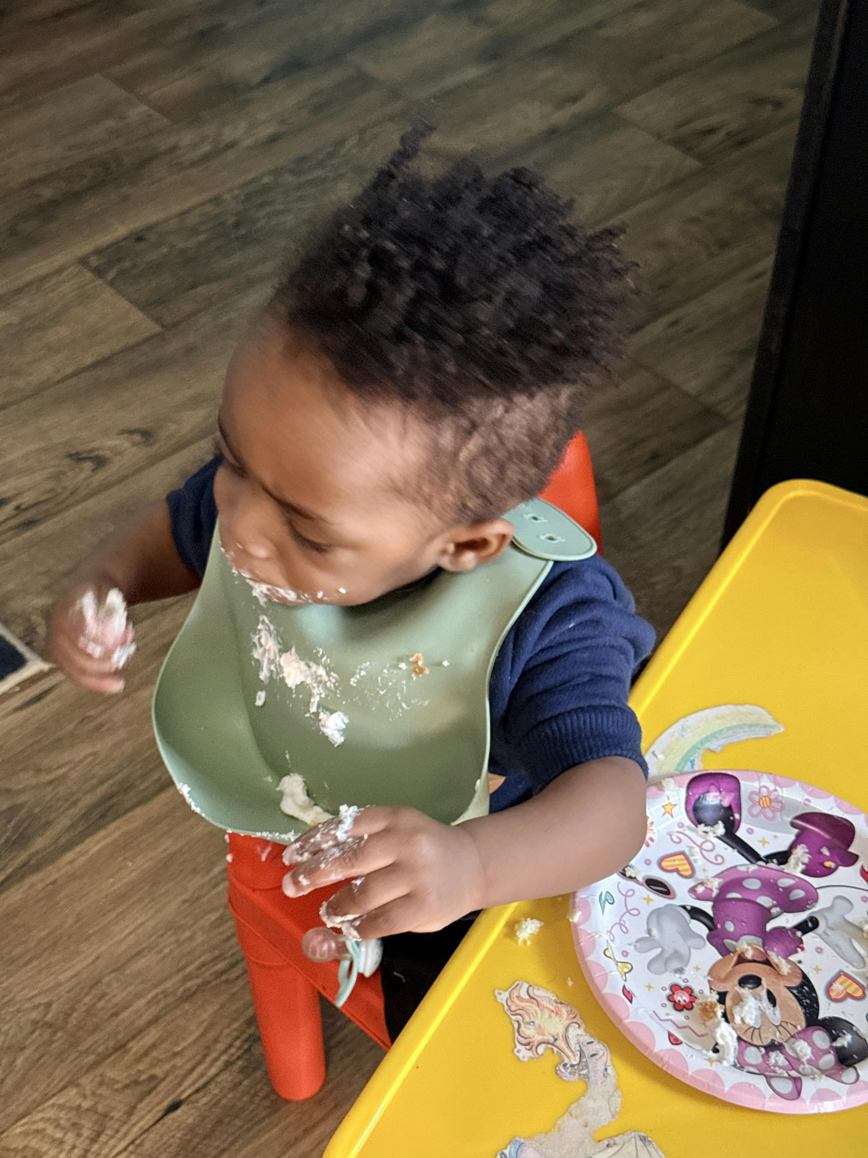 Child in a bib, hands and face covered in cake