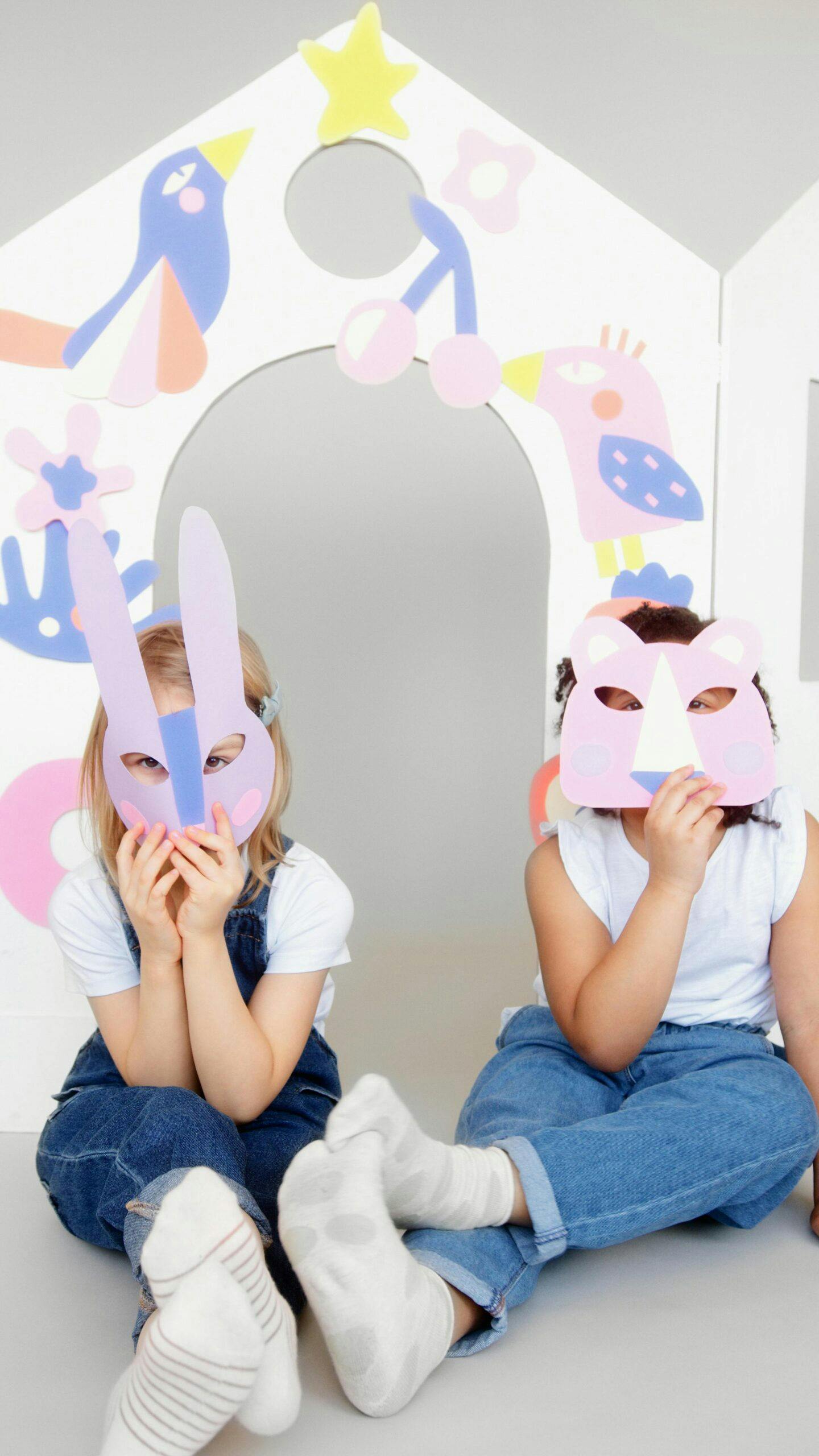 Two children wearing animal masks sitting in a playhouse cutout