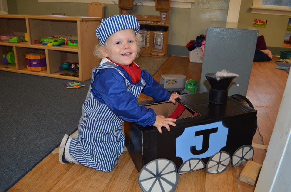 Child in a striped engineer costume kneeling next to a toy train