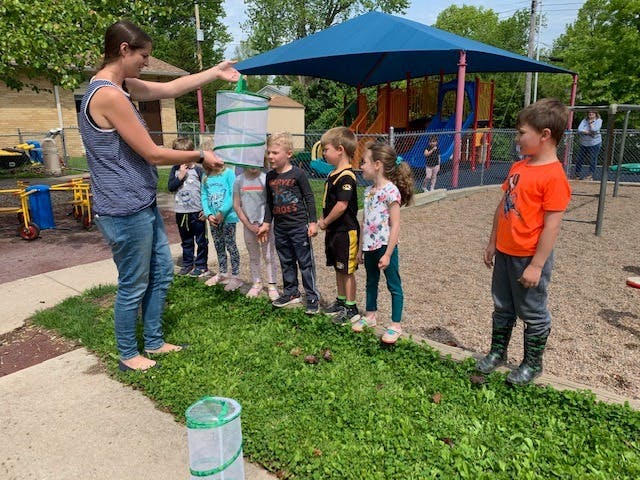Person showing children a bug net on a playground