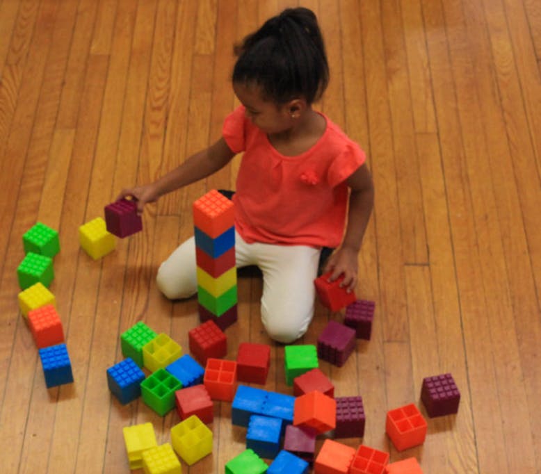 Child kneeling on floor playing with colorful building blocks