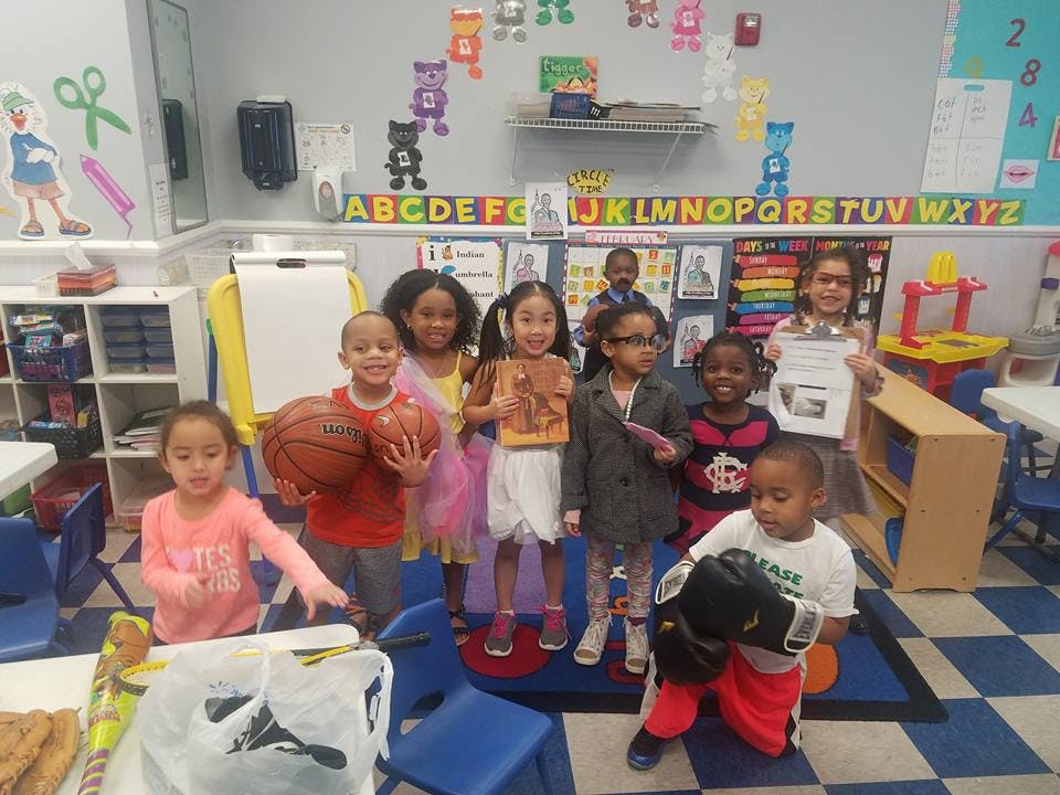 Group of children in a classroom, some holding basketballs, a book, or a paper