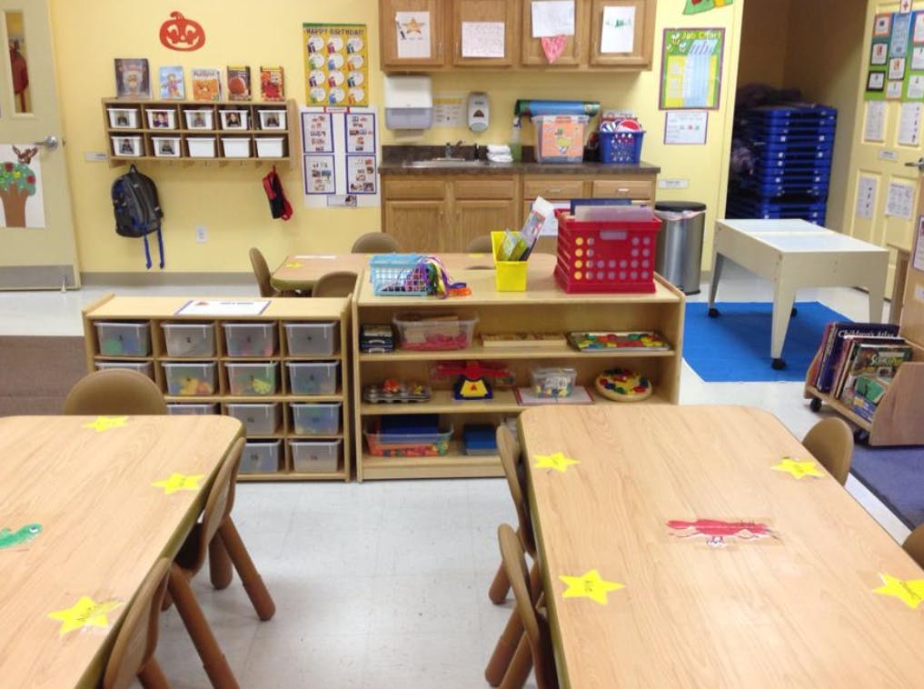 Classroom with small tables and chairs, shelves with storage bins and toys