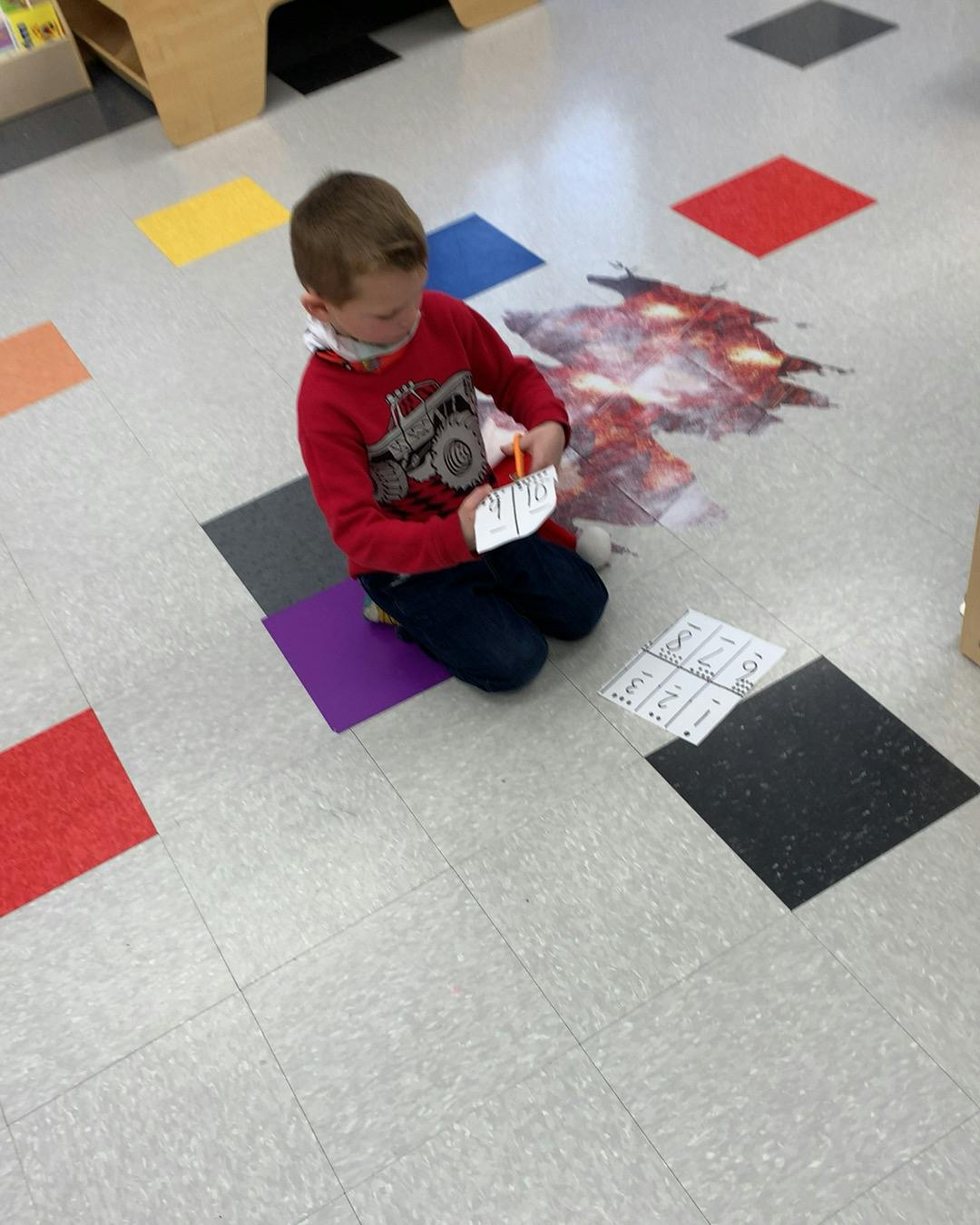 Child kneeling on floor cutting paper with scissors