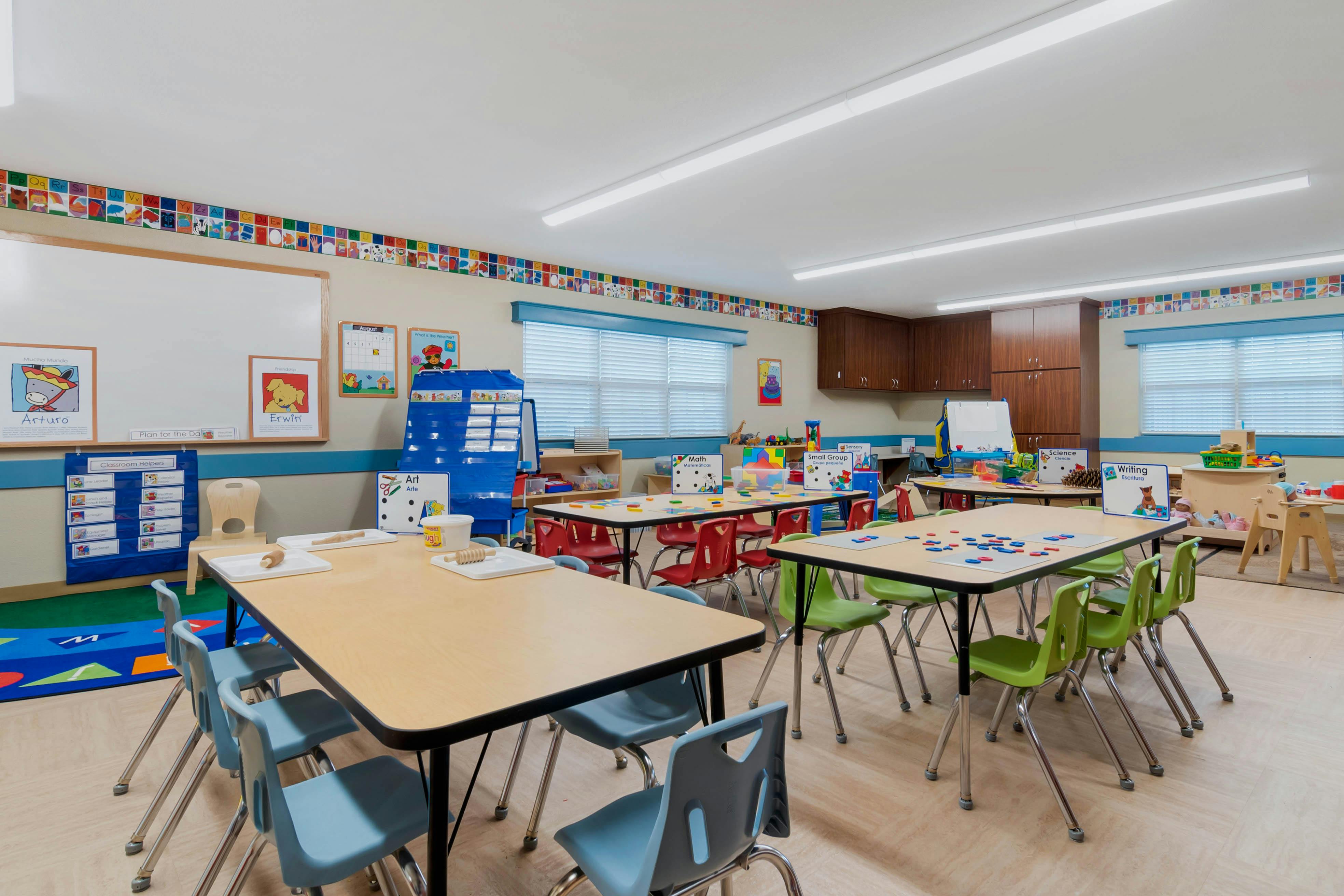 A colorful empty classroom with small tables and chairs arranged for children