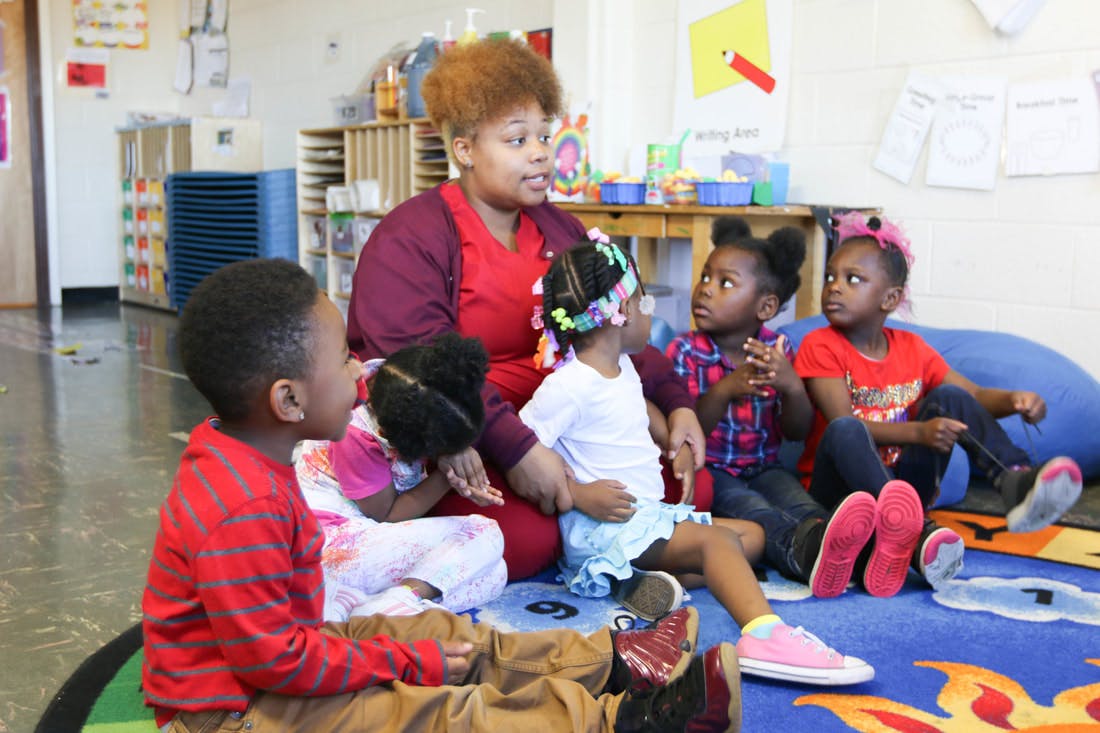 Adult person sitting on floor with several children in a classroom