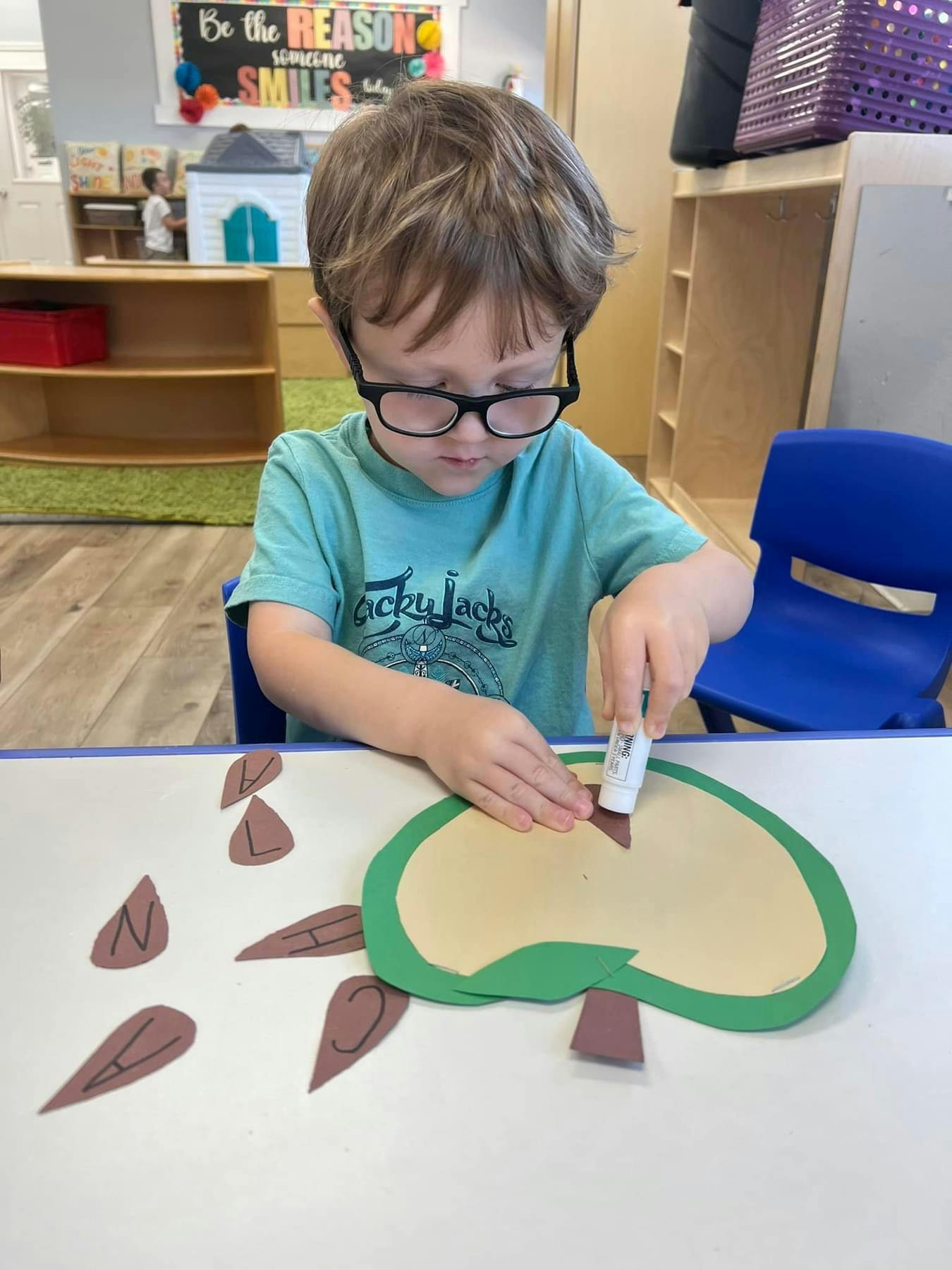 Child in glasses gluing paper cutouts onto a larger paper shape