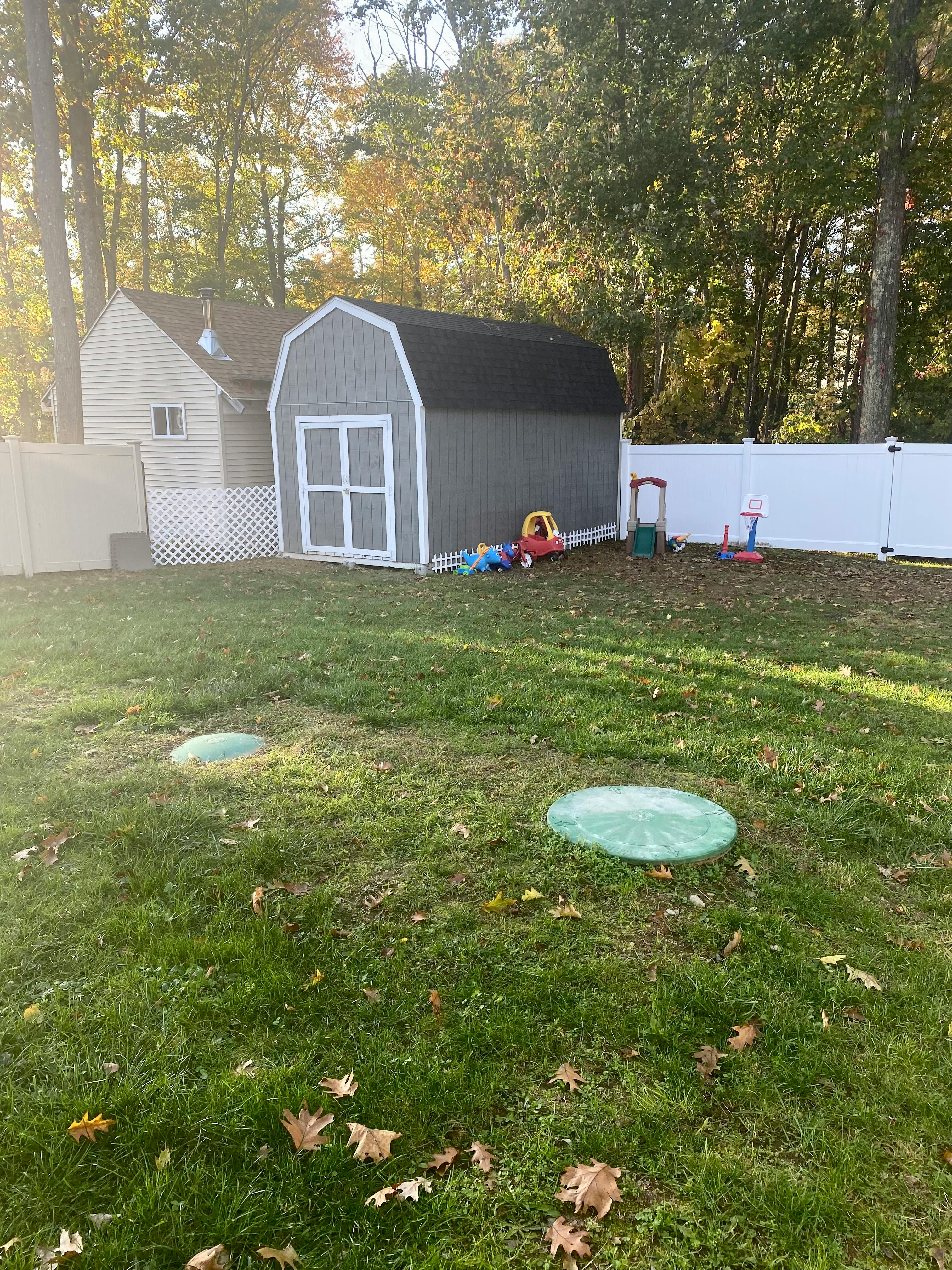 Gray shed with white trim in a backyard with a white fence