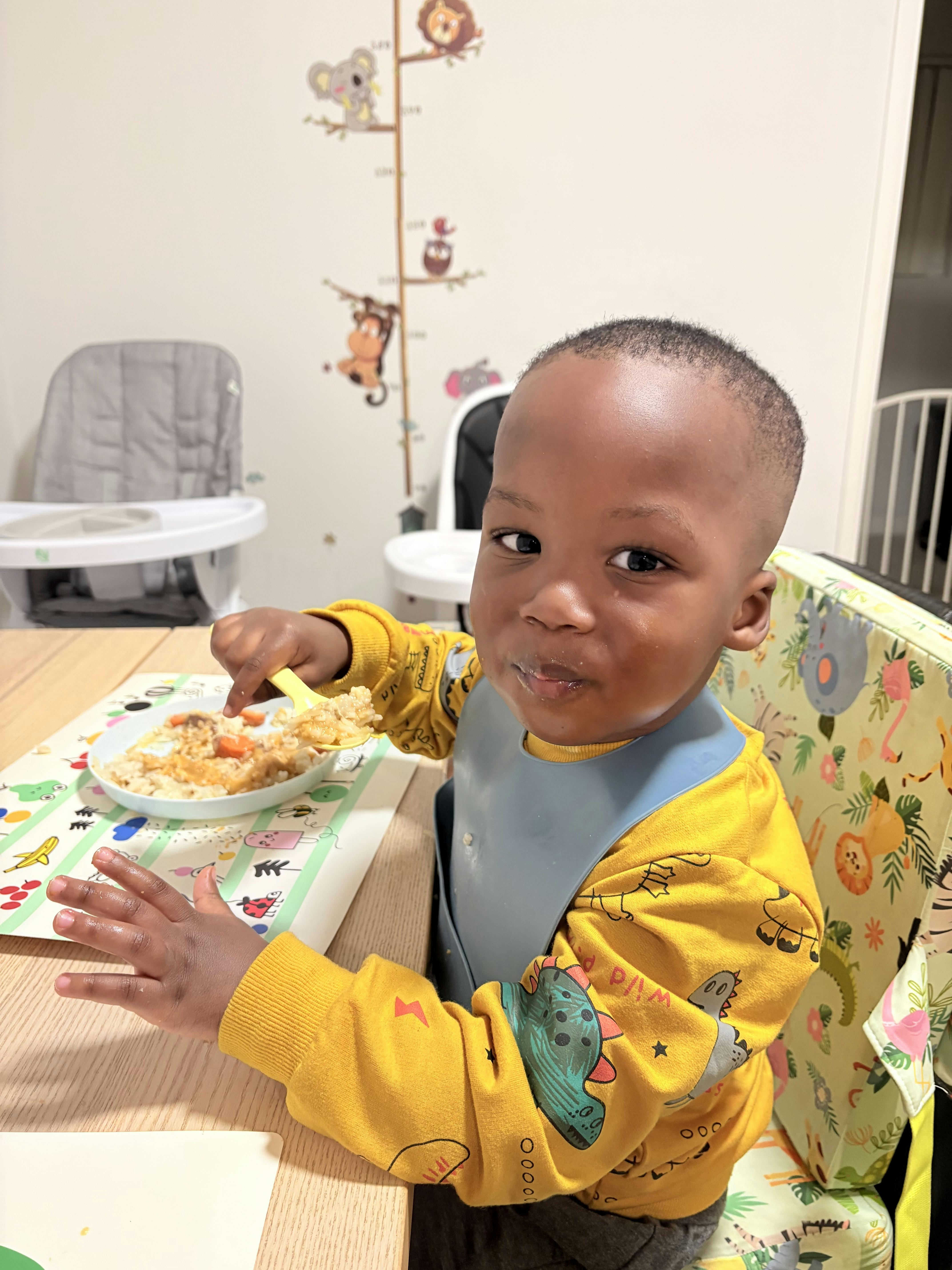 A young child wearing a bib eating a meal from a bowl at a table