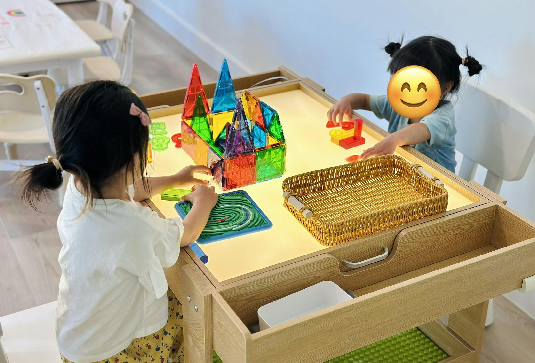 Two children playing with colorful magnetic blocks on a light table