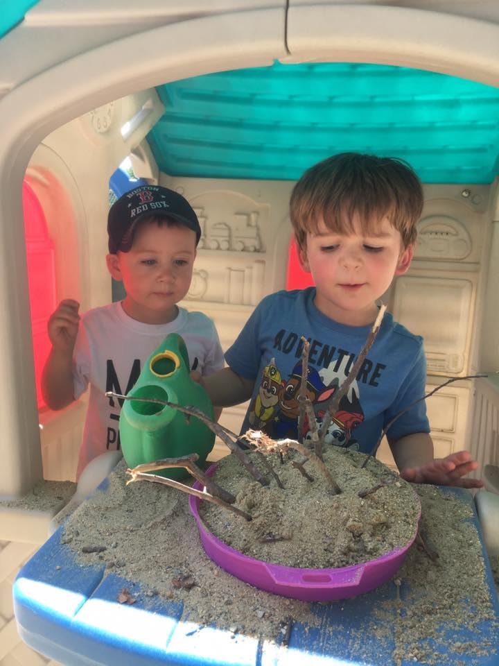 Two children playing with sand and sticks in a playhouse