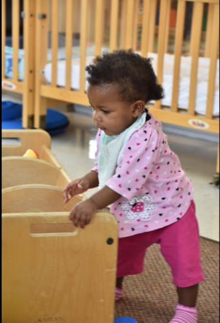 Child standing and holding onto a wooden toy