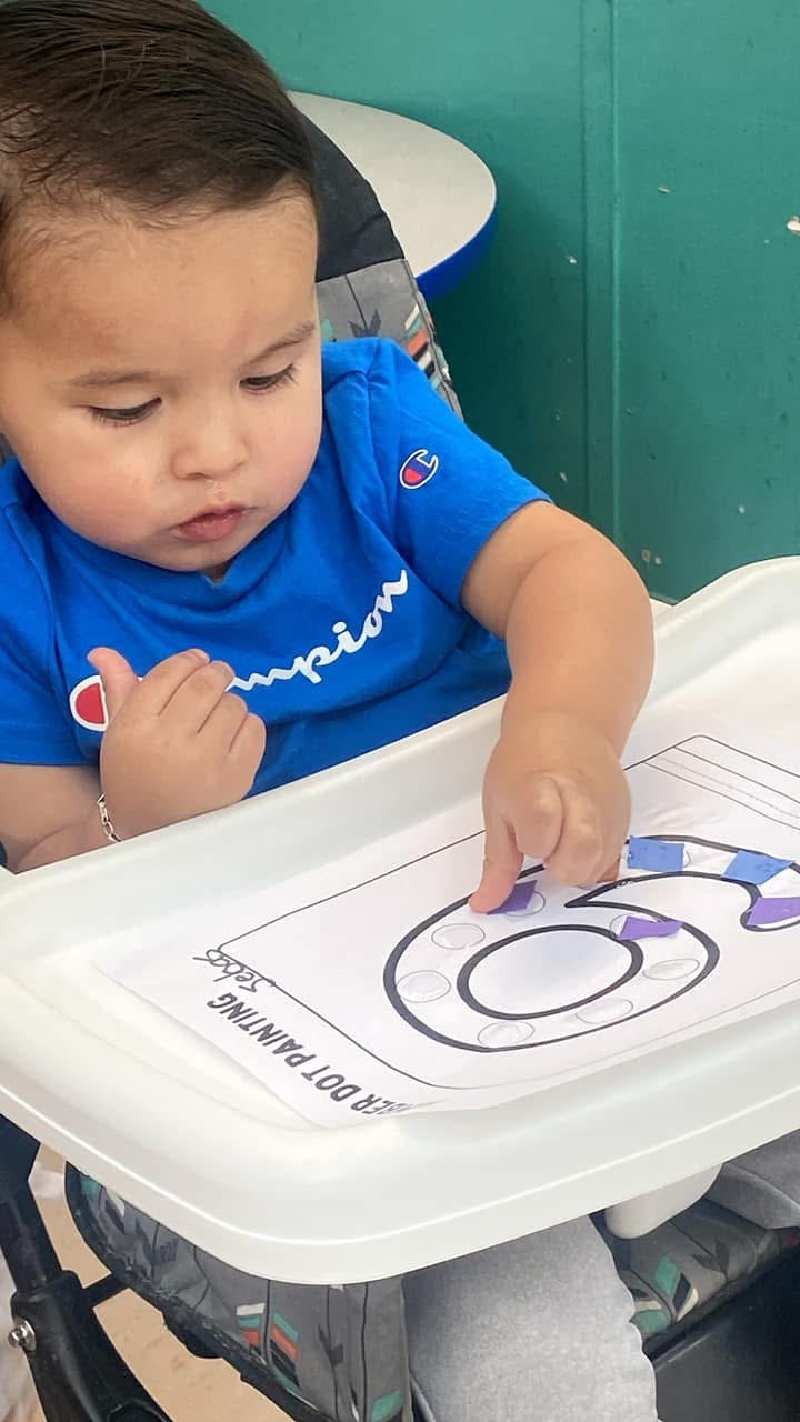 Child in a high chair doing a dot painting activity
