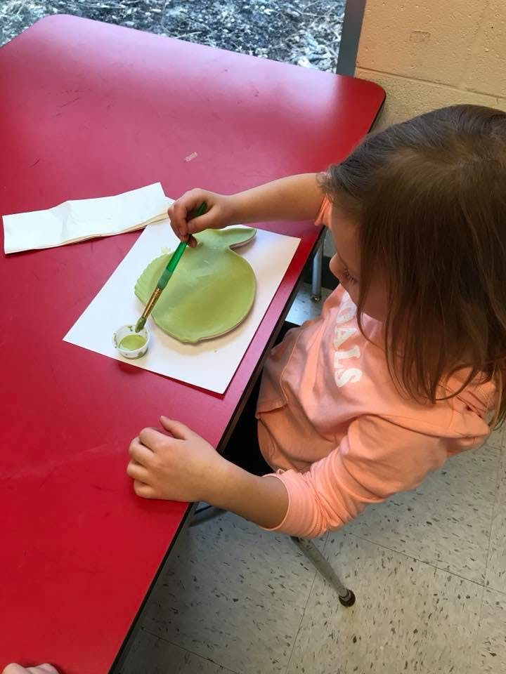 Child painting a green apple cutout at a red table