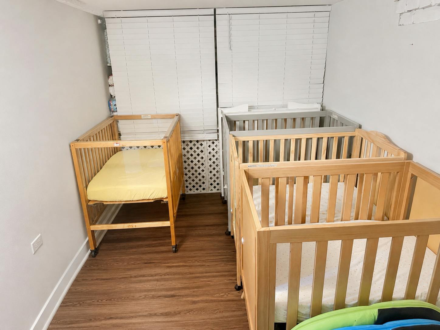 Three wooden cribs arranged in a room with hardwood floors
