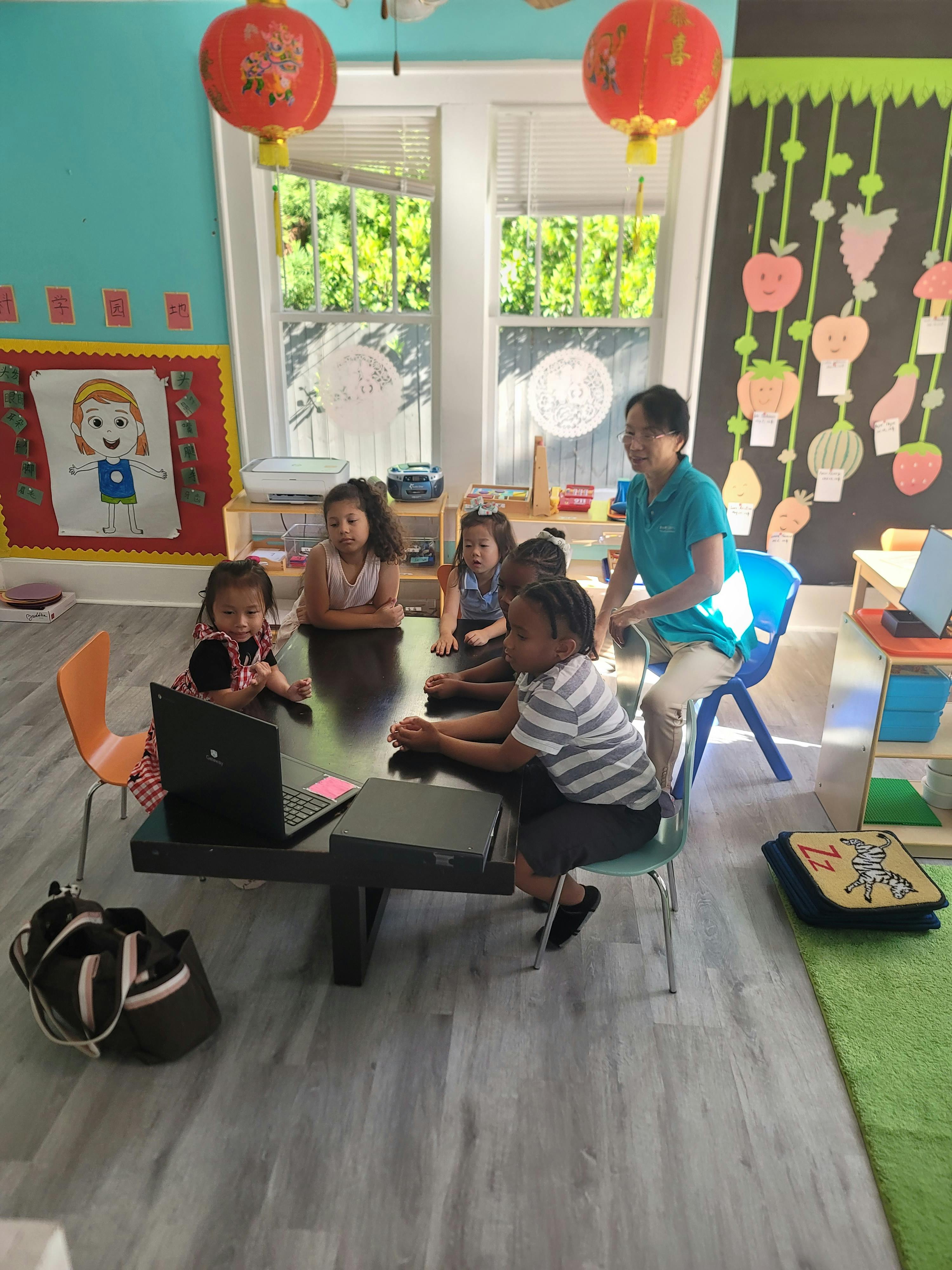 Adult and children gathered around a table with a laptop in a classroom