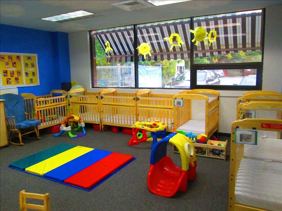 A room with multiple wooden cribs, a colorful playmat, and a small slide