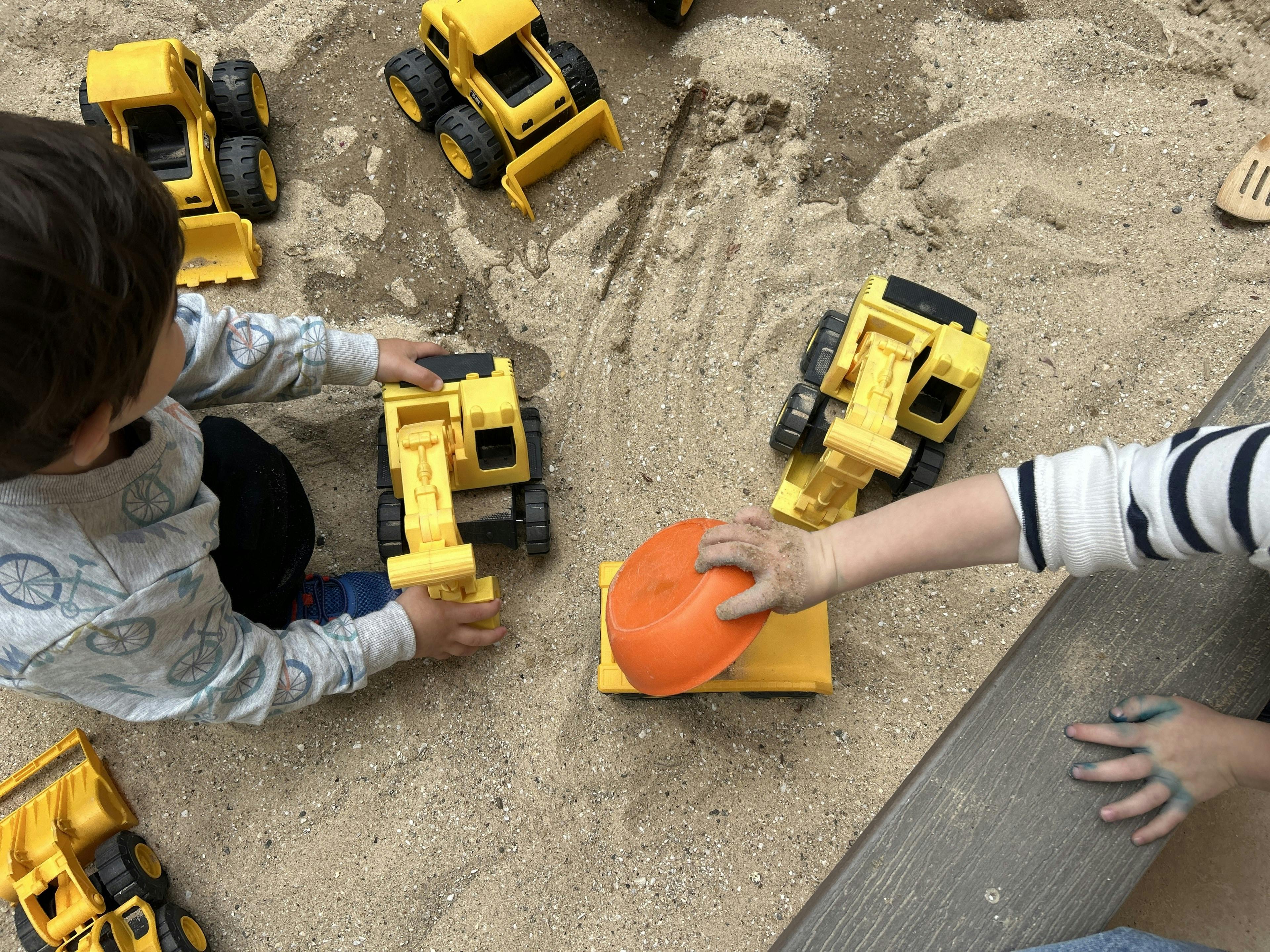 Two children playing with toy construction vehicles in sand