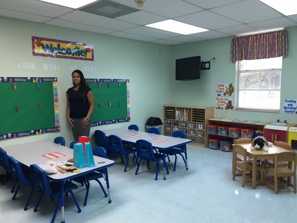 Person standing in a classroom with small tables and chairs