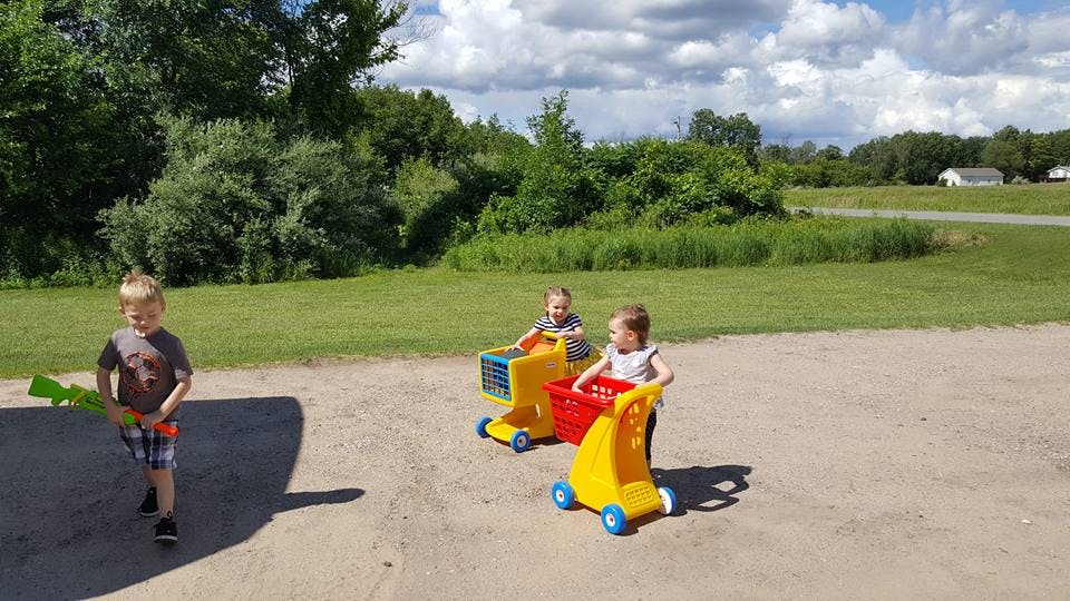 Three children playing outdoors, two with toy shopping carts