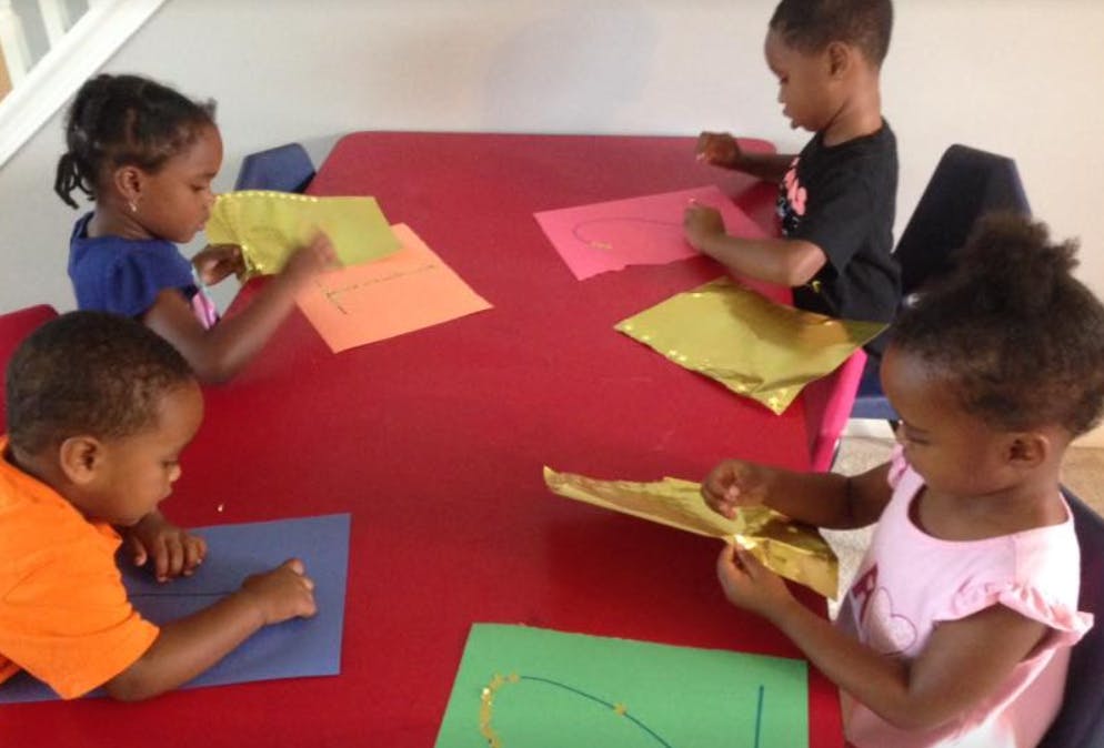 Four children sitting at a red table with colorful paper
