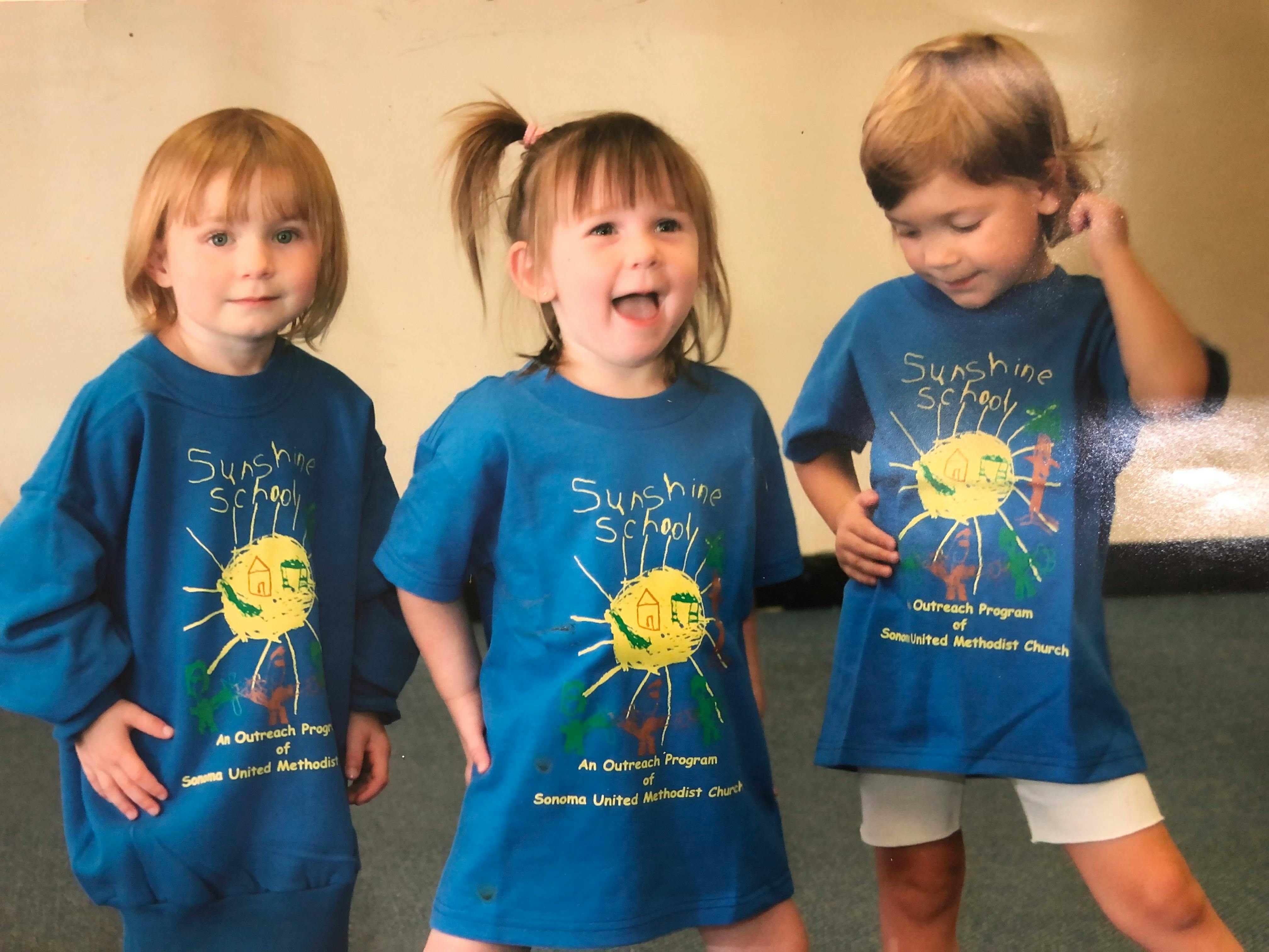 Three children wearing blue shirts with a yellow sun design