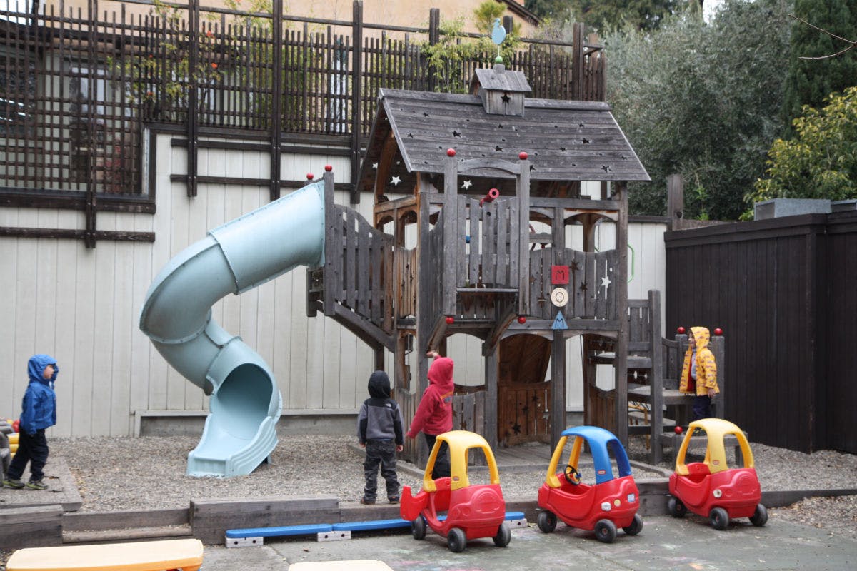 Children playing on a playground with a slide and toy cars