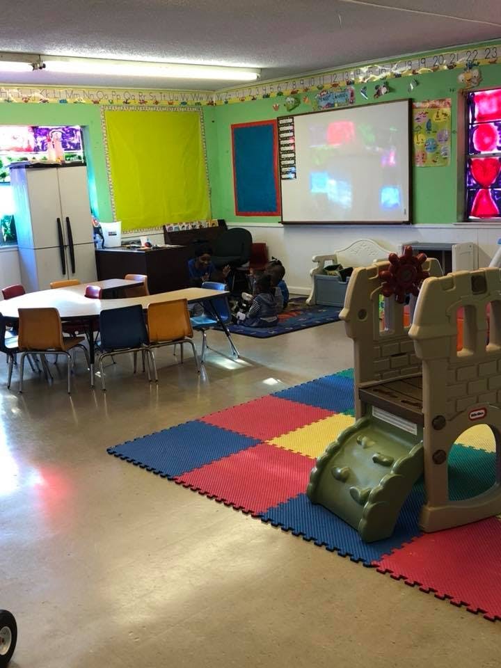 Classroom with tables, chairs, play structure, and a person sitting on the floor