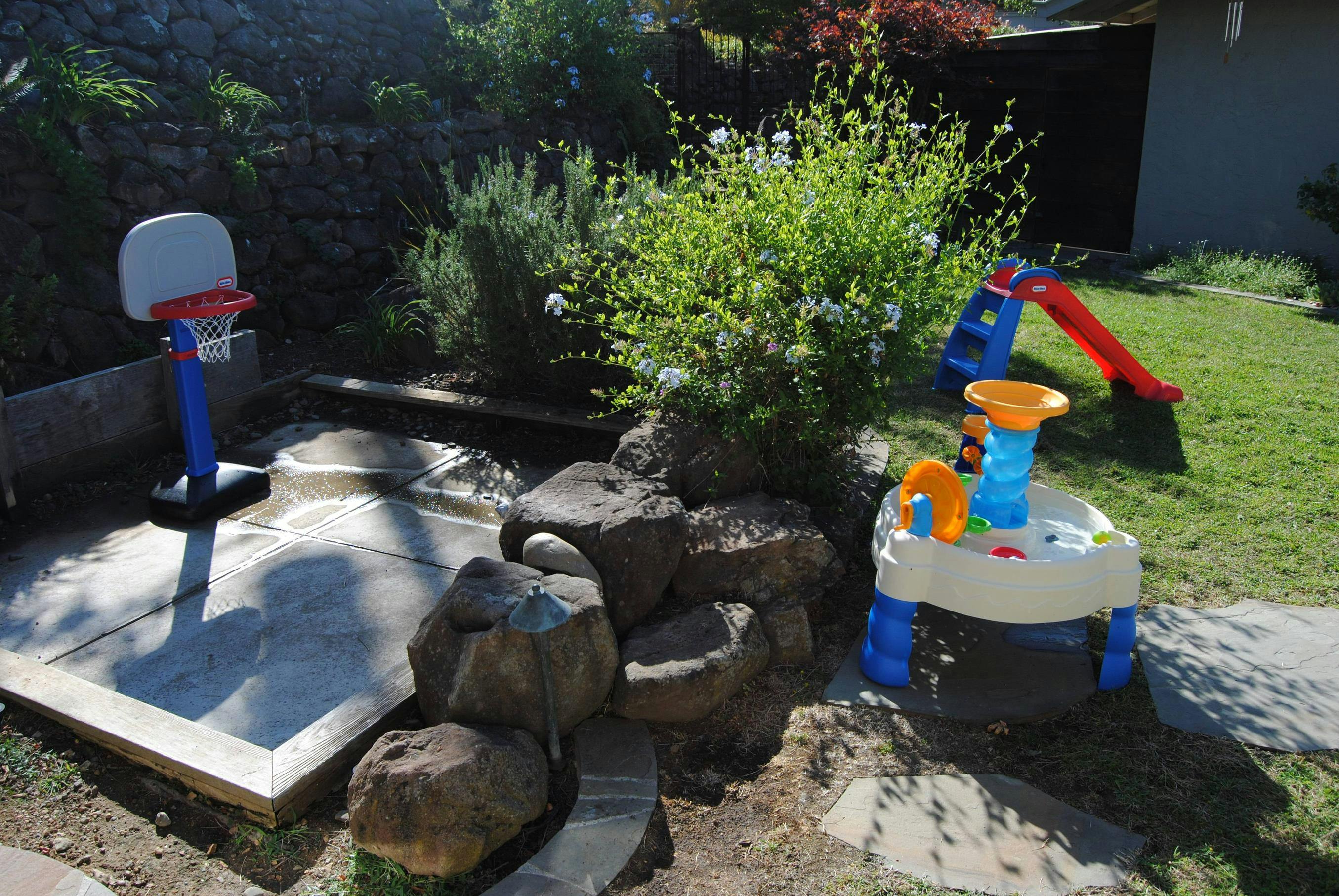 Backyard with a sandbox, small basketball hoop, water table, and slide