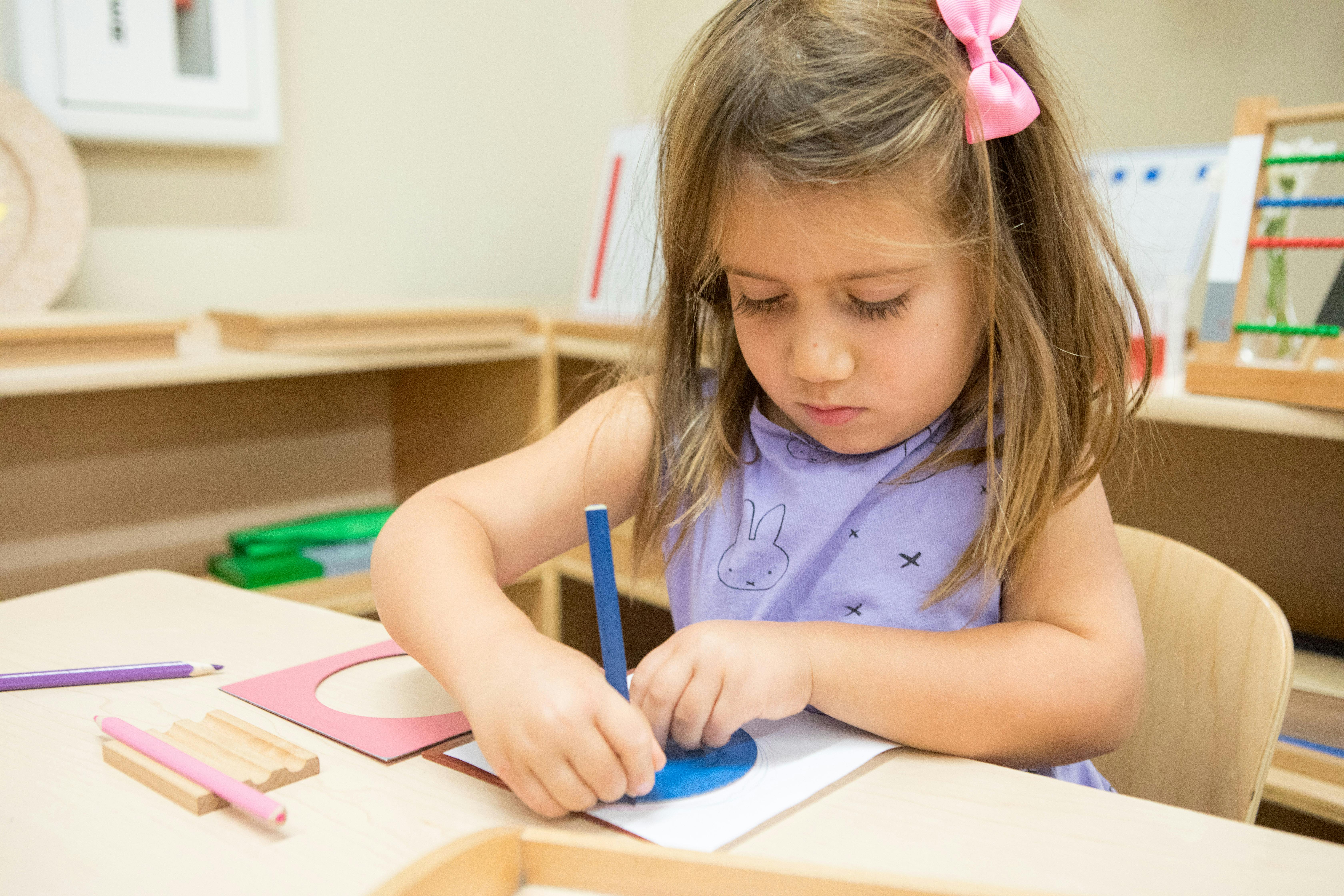 Child drawing on paper with a blue stencil and pink stencil