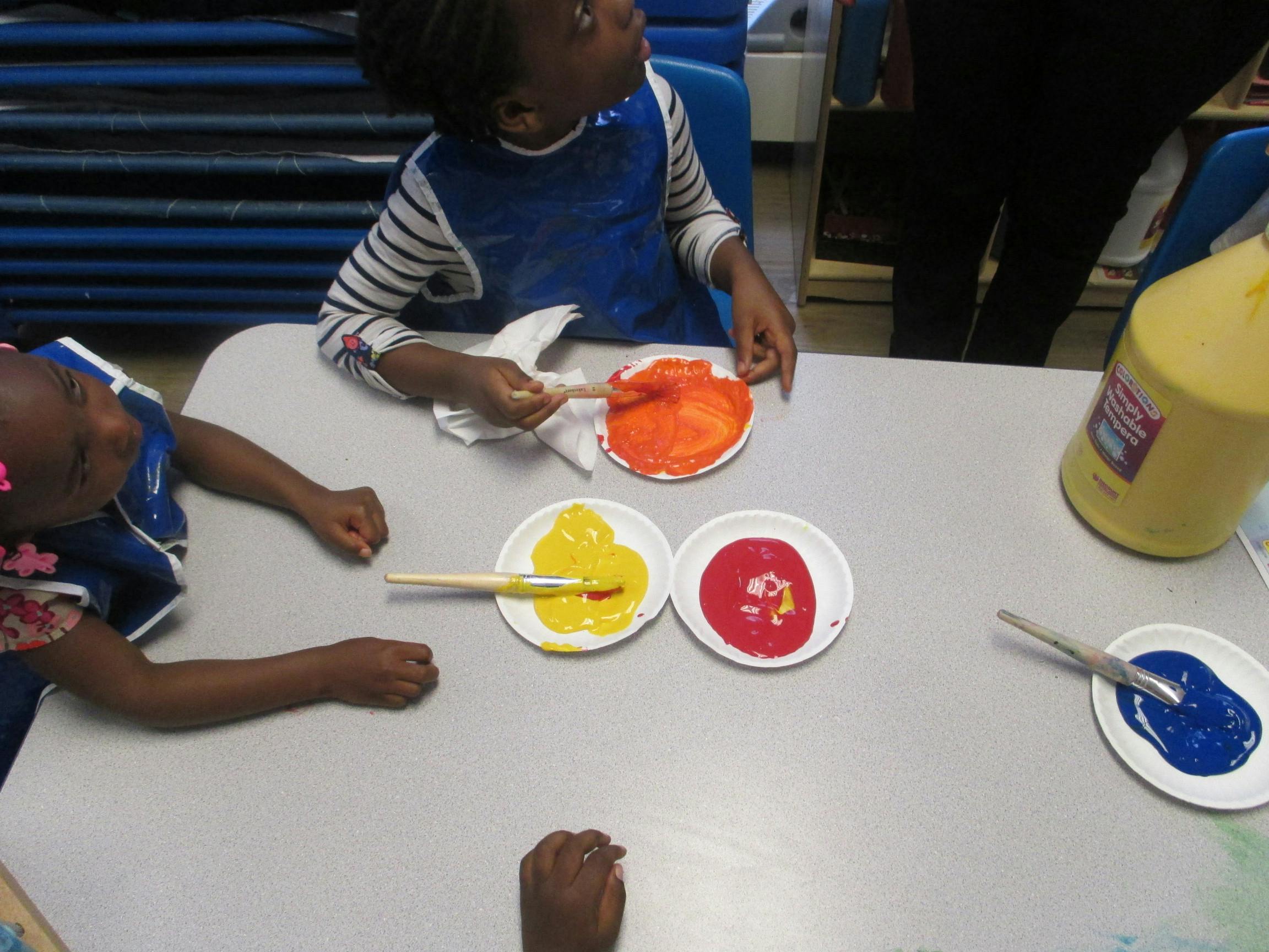 Child painting with orange, yellow, red, and blue paint