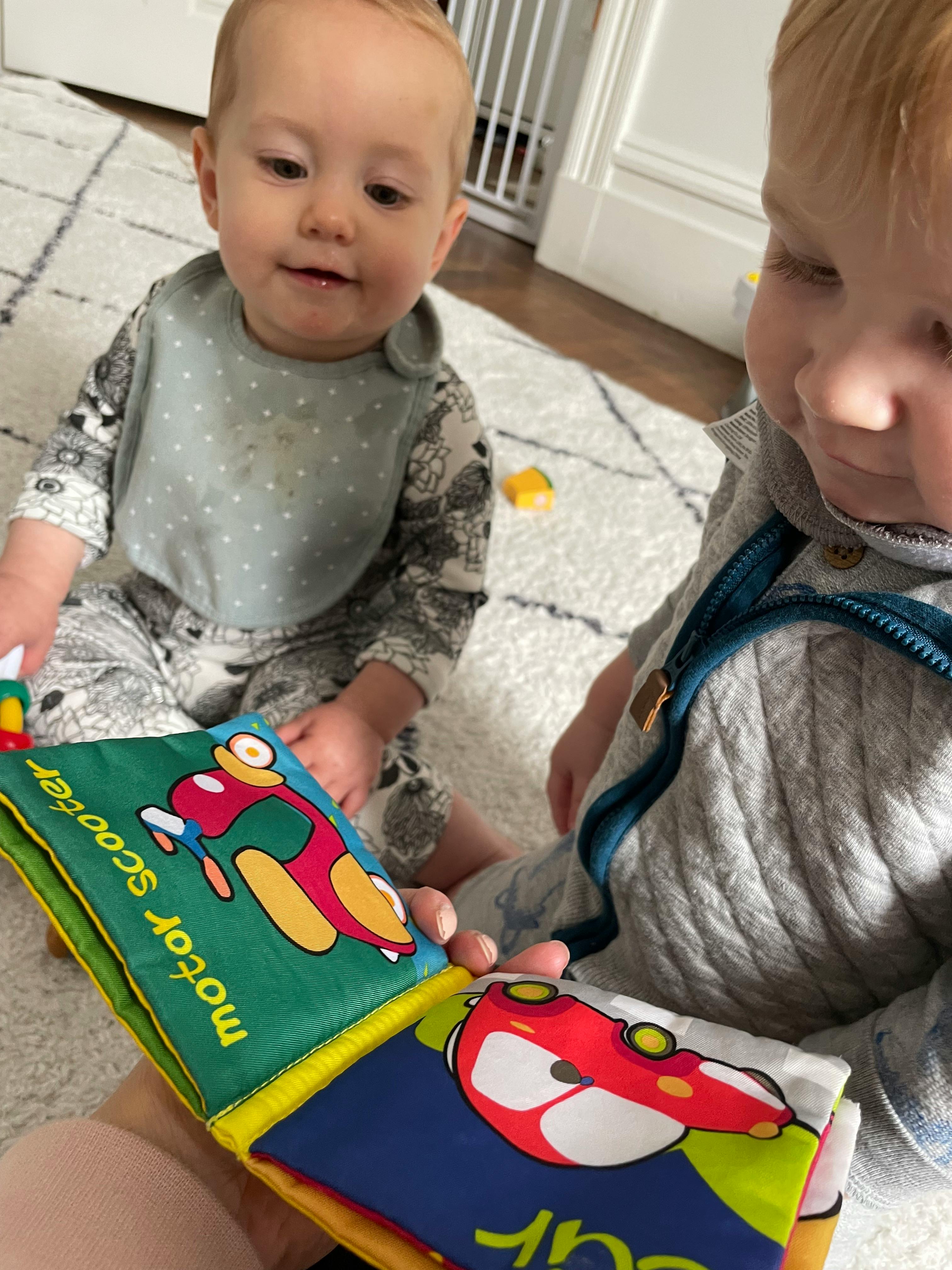 Two children looking at a soft fabric book with vehicle illustrations