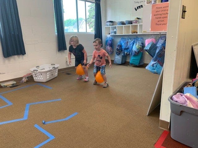Two children walking with orange balloons in a classroom