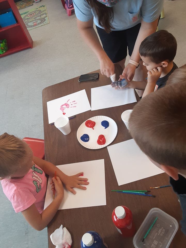 Adult helping children with handprint painting at a table
