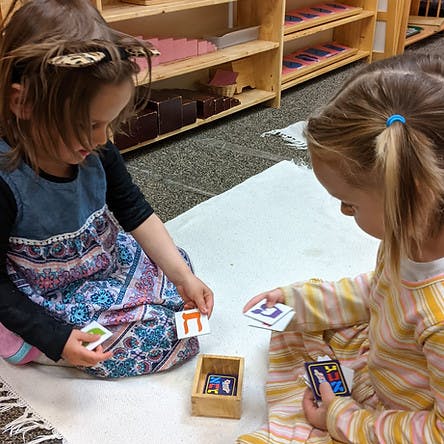 Two children playing with alphabet letter cards on the floor