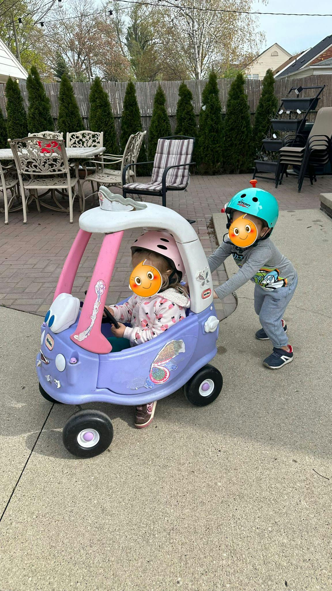 Child in toy car pushed by another child wearing a helmet