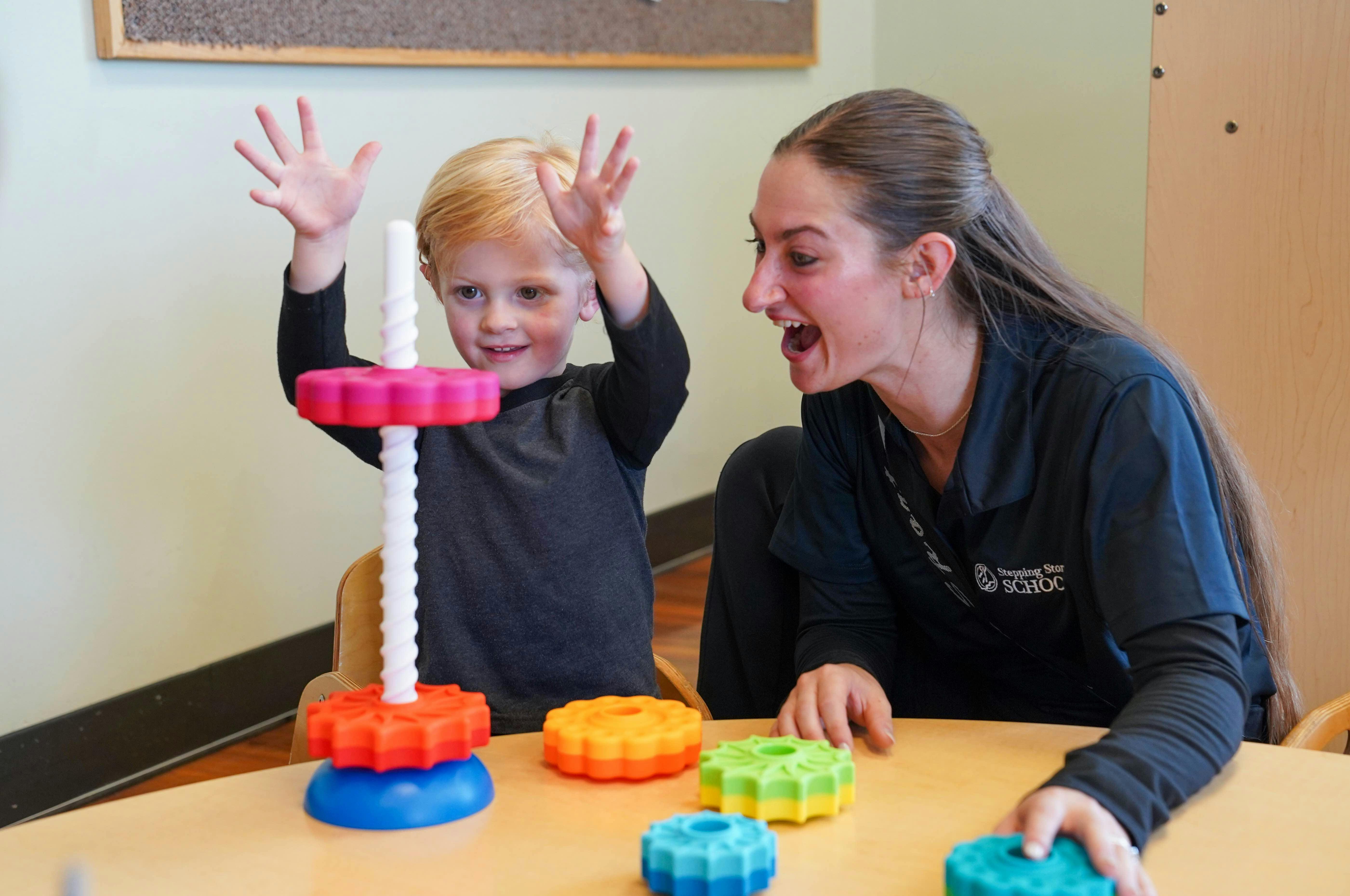 Child and adult playing with colorful stacking toys at a table