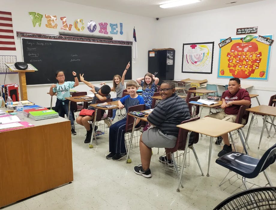 Children in a classroom, some raising their hands