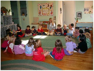 Adult and children sitting in a circle on a rug in a classroom