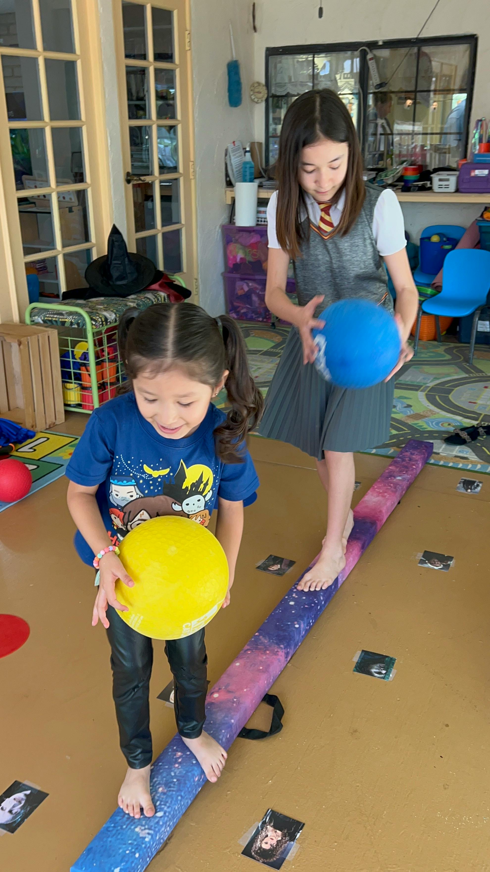 Two children balancing on a beam while holding balls